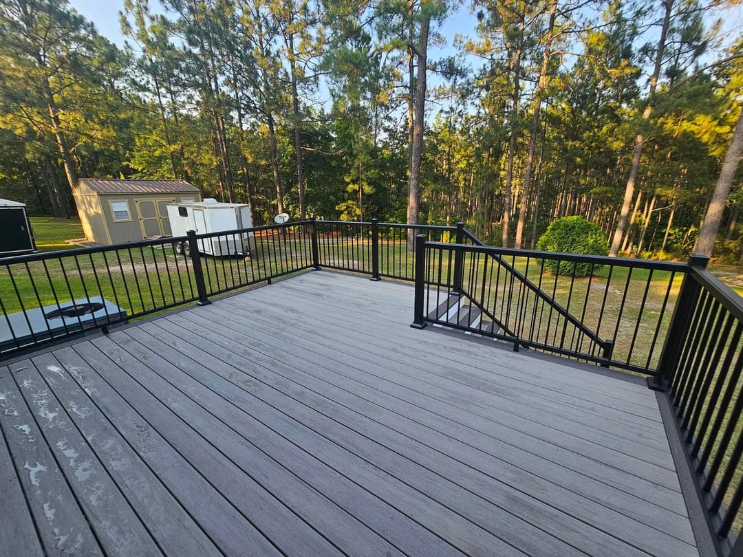 Spacious deck overlooking a wooded area with green trees and a storage shed.