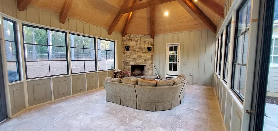 Cozy sunroom with stone fireplace, vaulted wooden ceiling, and spacious seating area.